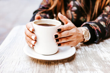 woman hand holding a cup of coffee outdoors at coffee shop or cafe with blurred background