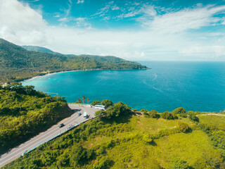 Fototapeta na wymiar Aerial view of road in beautiful green forest and sea coast in Lombok Island, Indonesia. Colorful landscape with cars on roadway, blue water and trees in summer