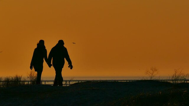 Silhouettes of a couple walking at the beach in the sunset.