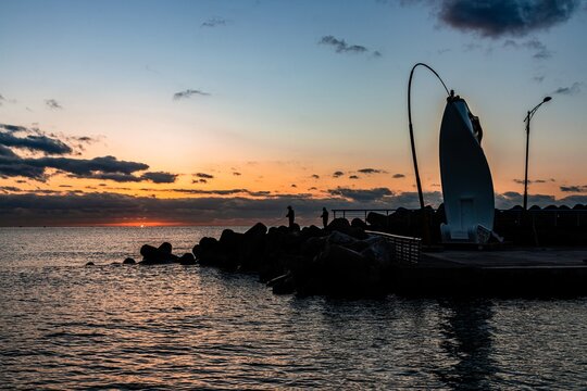 Silhouette Of Two Males Fishing On A Seashore During Sunset