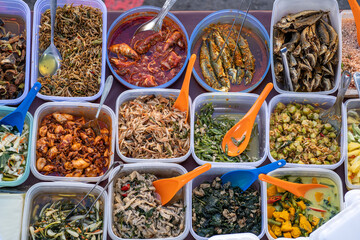 Overhead shot of people buying food over variety of delicious Malaysian home cooked dishes sold at...