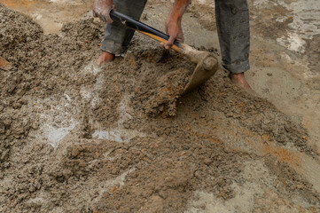 Indian labour mixing cement and water manually on floor using a shovel. Stock image.