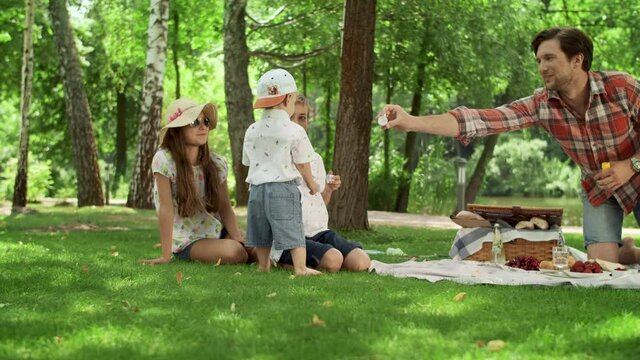 Positive parents blowing soap bubbles with children in park