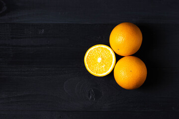 Two fresh oranges and one cut on the dark wood background
