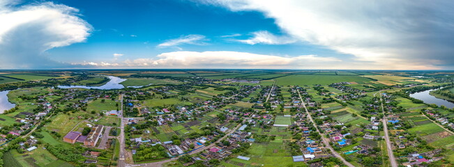 Bratsky farm in the south of Russia, surrounded by fields near a flat river with a dam -  t aerial panorama with a sunny and rainy day