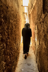 Unidentifiable man in a djellaba, berber clothing walking down a narrow street in Fes Medina in...