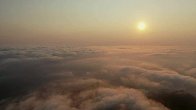 Aerial shot of cloudscape and sun over mountains during sunset, drone flying forward over famous Mount Warning against orange sky