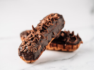 Homemade eclairs with chocolate on white marble background. Close up view of delicious healthy profitroles with chocolate glaze