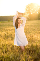 Fototapeta na wymiar Beautiful young woman wearing white dress in wheat field relaxing. Glow sun