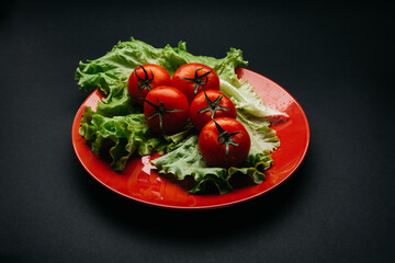 Fresh tomatoes with drops of water and lettuce on a red plate on a dark background