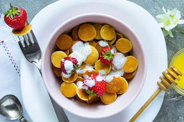 Trendy food - pancake cereal. Heap of mini cereal pancakes with strawberries. Top view or flat lay.