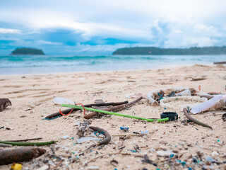 Fototapeta na wymiar Environmental pollution. Ecological problem. Garbages, plastic, and wastes on the sandy beach of tropical sea. Island and mountain background.