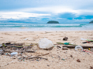 Environmental pollution. Ecological problem. Garbages, plastic, and wastes on the sandy beach of tropical sea. Island and mountain background.