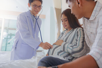 Doctor using stethoscope for examining pregnant woman with her husband at hospital