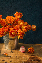 bucket of orange tulips on a wooden table on a dark background