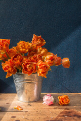 bucket of orange tulips on a wooden table on a dark background