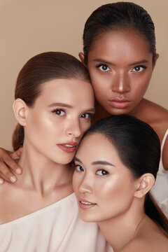 Beauty. Diverse Models Portrait. Tender Caucasian, Asian And Mixed Race Women Posing Together On Beige Background. Female With Perfect Skin And Natural Makeup Looking At Camera.