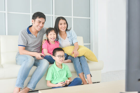 Happy asian family sitting on sofa and watching movie on TV together at home.