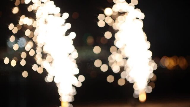 Two small white firework burning and exploding - spreads sparkles on the beach - unfocused