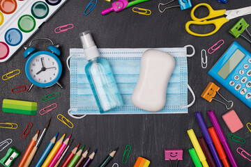 Staying healthy and educated concept. Top above overhead view photo of colorful stationery with mask soap and hand sanitizer in center isolated on blackboard