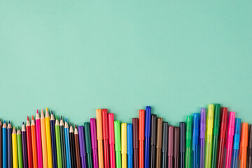 Obraz premium Top above overhead view flatlay photo of multicolored crayons pens and markers isolated on turquoise background with copyspace