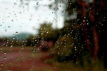 Water rain drops on car transparent glass window with tropical summer rainforest green plants & trees background in rainy season, Eco environment & exotic travel concept    