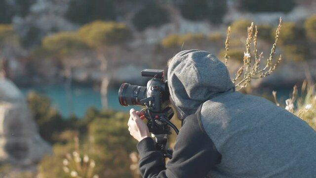 Photographer sets up his camera and looks through the finder of the camera on a tripod in a beautiful scenery at the bay "Calo des Moro" in the balearic island Mallorca, Spain - Slow Motion