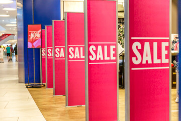 Discount in mall banner. A row of pink light boxes with an ad at the entrance to the store. Seasonal sale. Blurred.