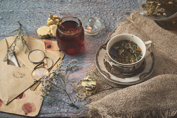 Cozy morning at home - old book and romantic letters to read, cup of delicious herbal tea with ginger and a jar of forest honey