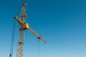 Fototapeta premium Top of a yellow construction hoisting crane against a blue sky background.