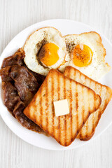 Homemade Healthy Sunnyside Eggs Breakfast on a white plate on a white wooden table, top view. Flat lay, overhead, from above.