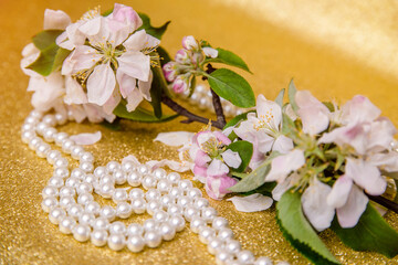 Fototapeta na wymiar Pearl necklace and Apple blossom branch on a Golden background 
