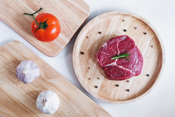 Raw meat, beef steak, on wooden board with tomato and garlic. Top view