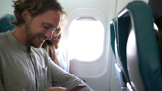 Couple in plane on travel taking selfie photo or video while flying on vacation travel. Two happy millennials taking pictures for social media going on honeymoon.