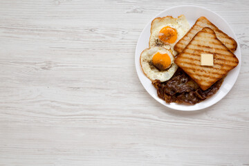 Homemade Healthy Sunnyside Eggs Breakfast on a white plate on a white wooden surface, top view. Flat lay, overhead, from above. Copy space.