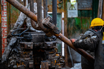 Two working drillers in a uniform, in a helmet and goggles, install drill pipes after lifting them...