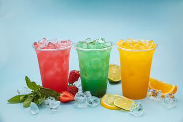 colored lemonades in plastic cups with ice, fruits and berries on a blue background
