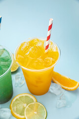 colored lemonades in plastic cups with ice, fruits and berries on a blue background
