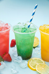 colored lemonades in plastic cups with ice, fruits and berries on a blue background
