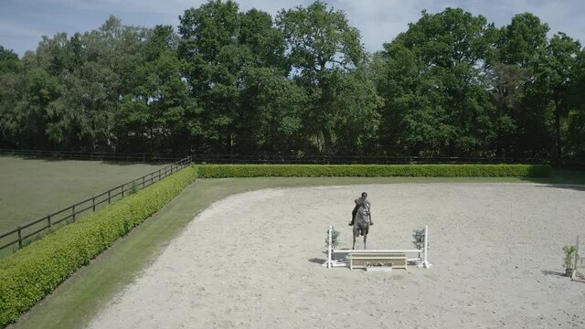 Pferd springt &uuml;ber Hindernis. Drohne verfolgt jungen Reiter. Sandplatz Parkour. Sprung