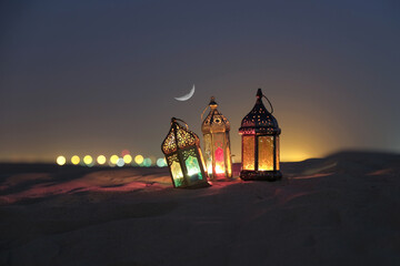Lantern in desert   lit against a crescent moon night sky during Ramadan Eid time