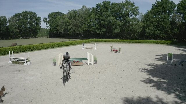 Pferd springt &uuml;ber Hindernis. Drohne verfolgt jungen Reiter. Sandplatz Parkour. Sprung