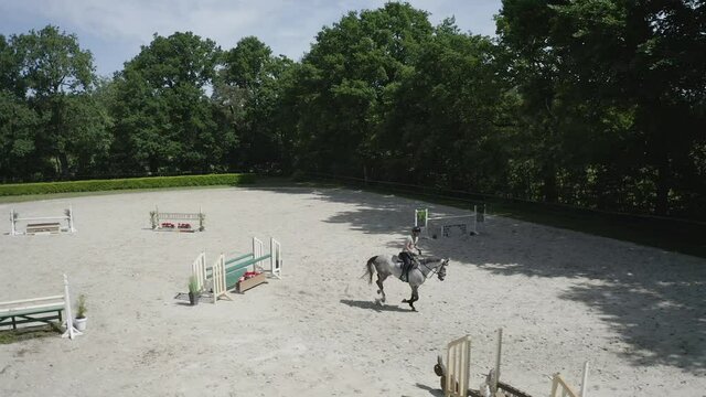 Pferd springt &uuml;ber Hindernis. Drohne verfolgt jungen Reiter. Sandplatz Parkour. Sprung