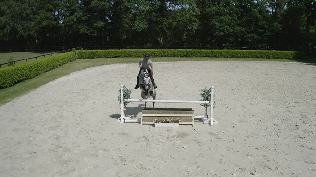 Pferd springt &uuml;ber Hindernis. Drohne verfolgt jungen Reiter. Sandplatz Parkour. Sprung