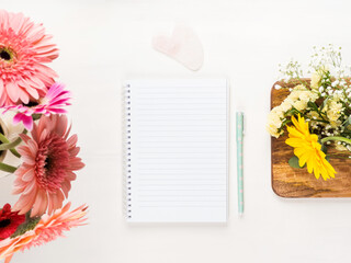 White open notebook and green pen with flowers around. Spring summer plan