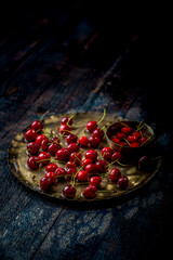 red and fresh cherries in old metal plate and bowl on dark wooden background with selective focus