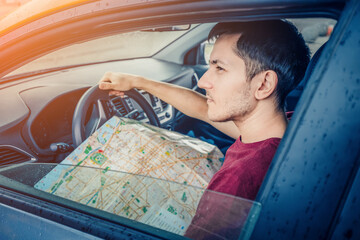 young man reads the map and looks for the destination driving his car. Travel and trip concept