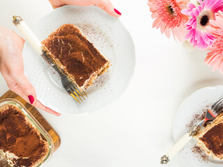 Traditional coffee tiramisu dessert with mascarpone cheese and cocoa powder served on plates on white wooden table. Female hands holding the plate