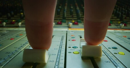Alternative angle macro slide shot of a sound producer hand is using a music mixer with editing tools in a professional recording studio.