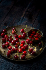 red and fresh cherries in old metal plate and bowl on dark wooden background with selective focus
